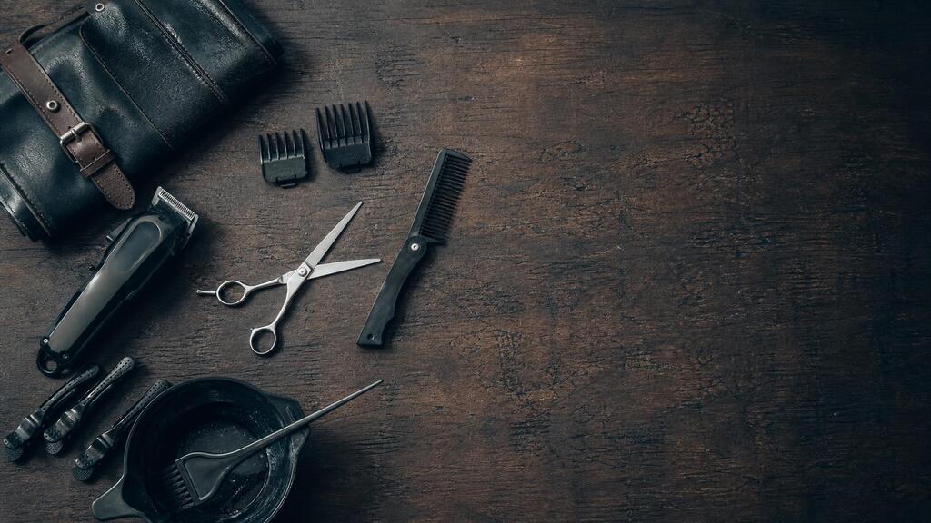 Overhead flat-lay of MyKey's house-call kit on dark worn wood — open shears, cordless clippers, combs, and a tint bowl